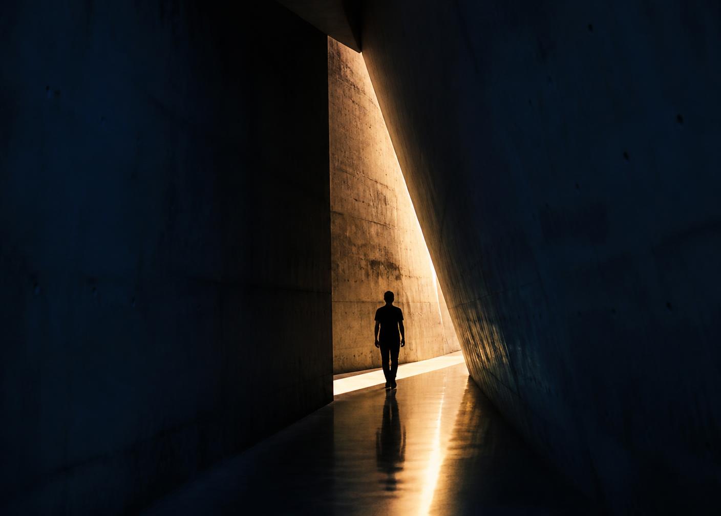 A lone figure walking through a concrete corridor toward a shaft of golden light